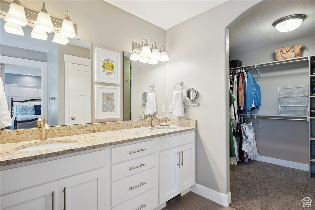 Ensuite bathroom with baseboards, a spacious closet, double vanity, and a sink