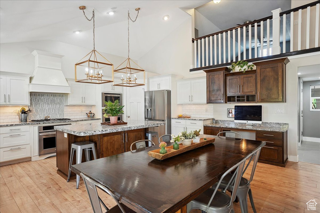 Kitchen featuring custom exhaust hood, light wood-style floors, appliances with stainless steel finishes, a kitchen island, and high vaulted ceiling