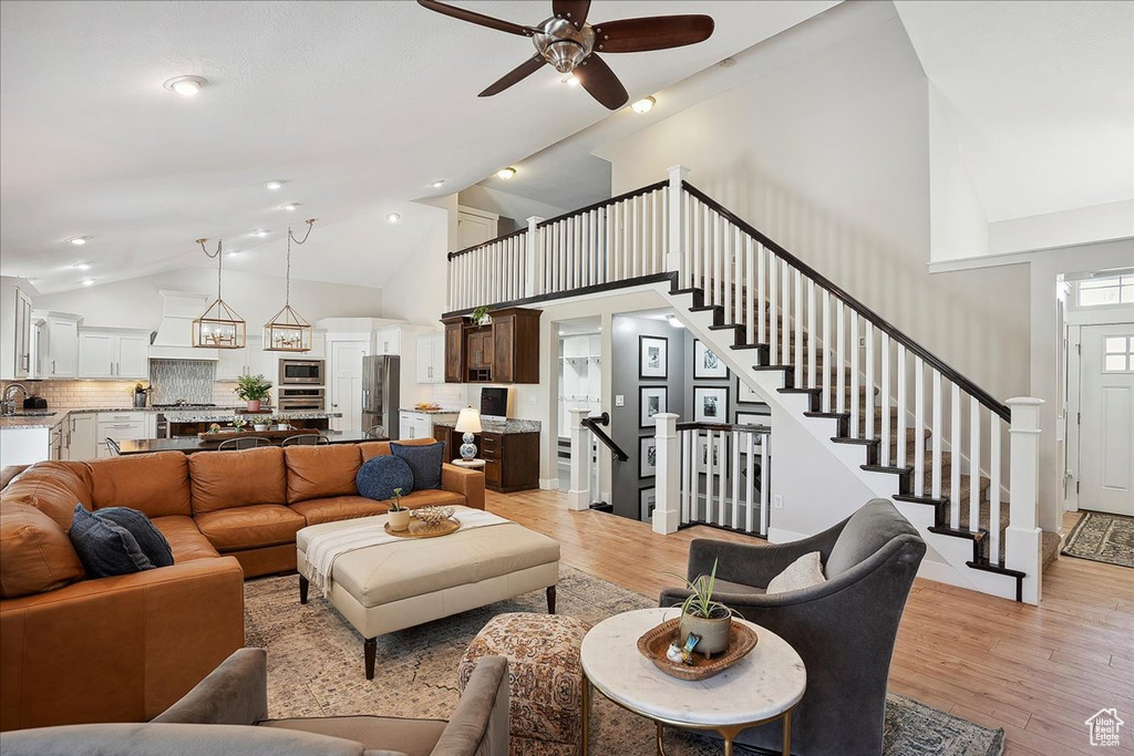 Living room with a ceiling fan, high vaulted ceiling, light wood-style flooring, and stairs