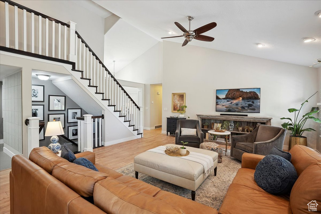 Living area with stairway, light wood-style floors, high vaulted ceiling, a ceiling fan, and baseboards