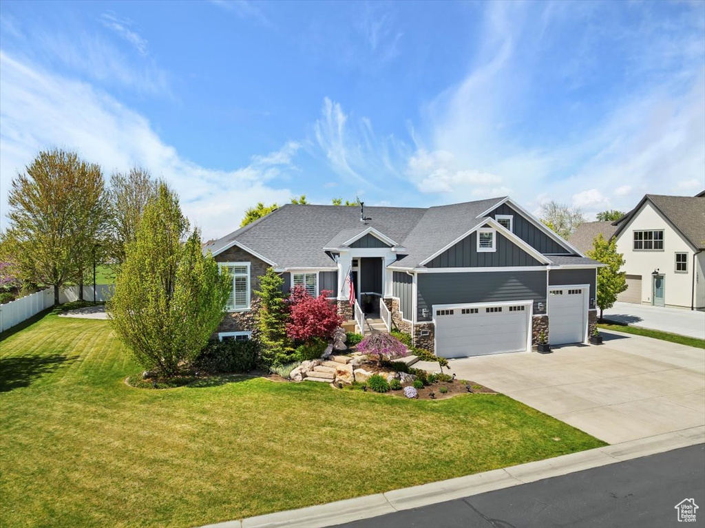Craftsman-style house with board and batten siding, concrete driveway, stone siding, a front yard, and a garage