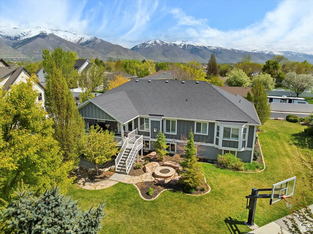 Back of house featuring a shingled roof, an outdoor fire pit, a lawn, stairs, and board and batten siding