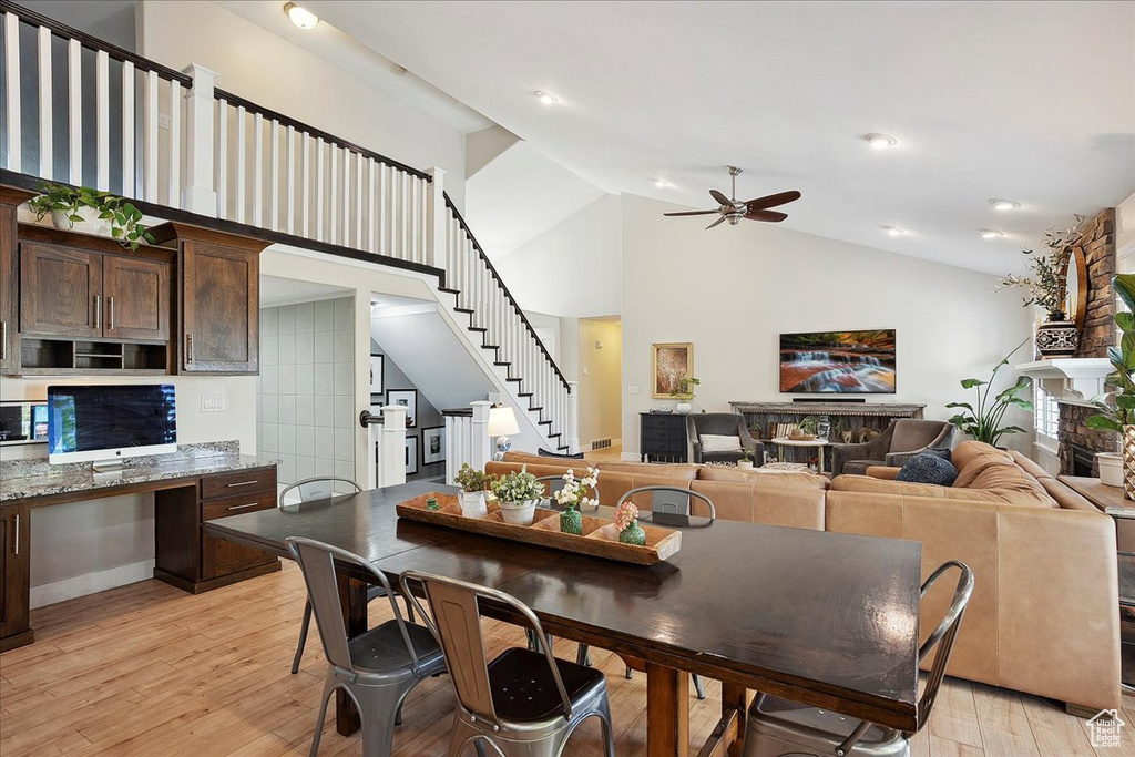 Dining area with stairway, a fireplace, light wood-style floors, high vaulted ceiling, and a ceiling fan