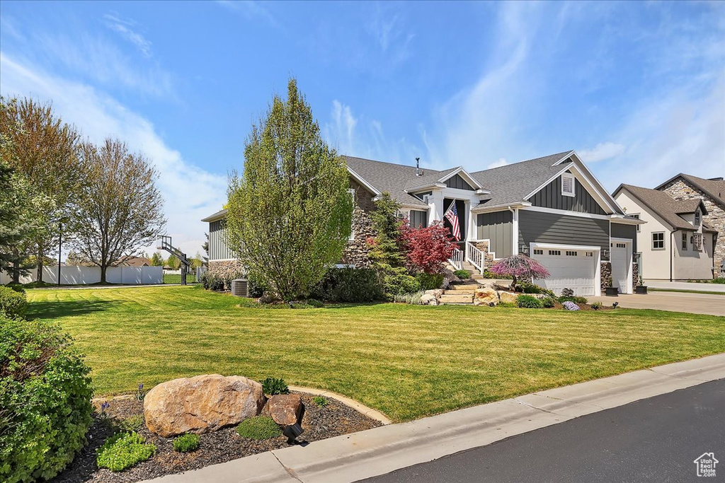 View of front of property with board and batten siding, concrete driveway, an attached garage, central AC unit, and a front lawn