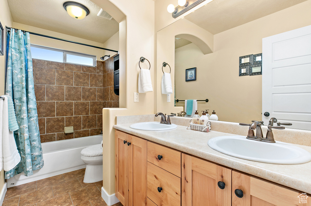 Full bathroom with double vanity, shower / tub combo with curtain, toilet, and a sink