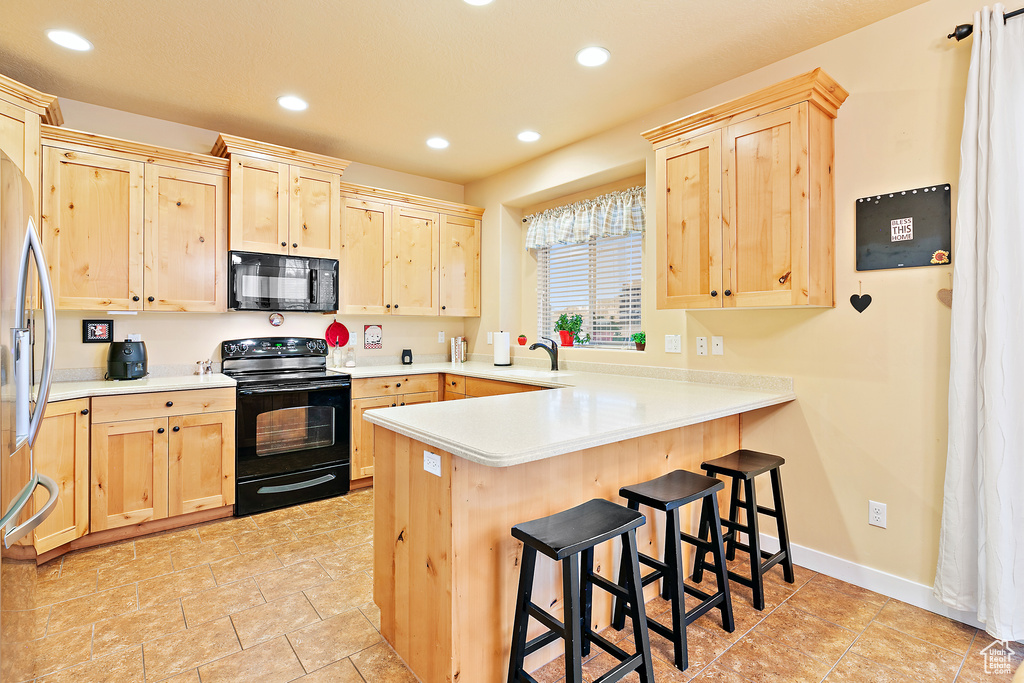 Kitchen featuring recessed lighting, light brown cabinets, a kitchen breakfast bar, black appliances, and a peninsula