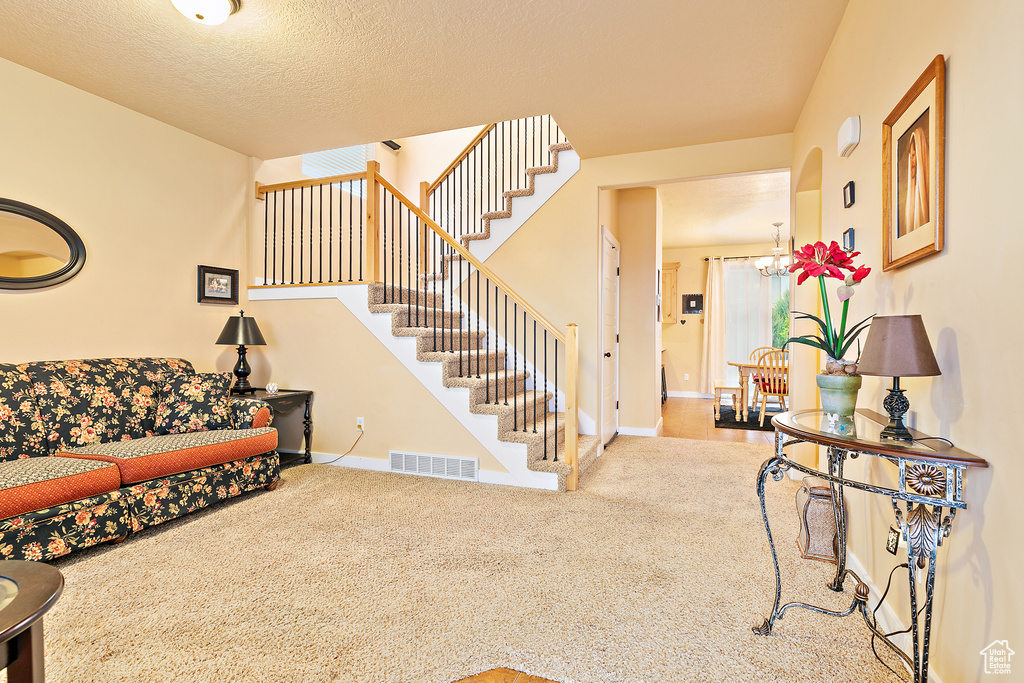 Carpeted living area with an inviting chandelier, stairway, visible vents, and baseboards
