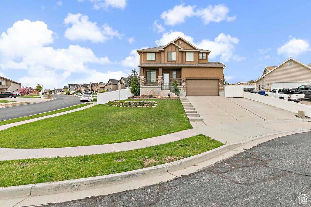 View of front of home featuring a front lawn, a residential view, stone siding, concrete driveway, and fence