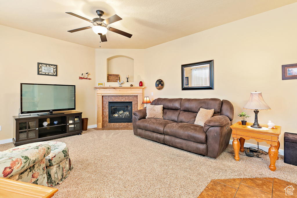 Carpeted living area featuring ceiling fan, a tiled fireplace, and baseboards