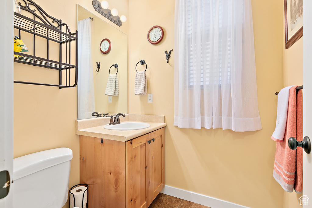 Half bath with toilet, tile patterned floors, vanity, and baseboards