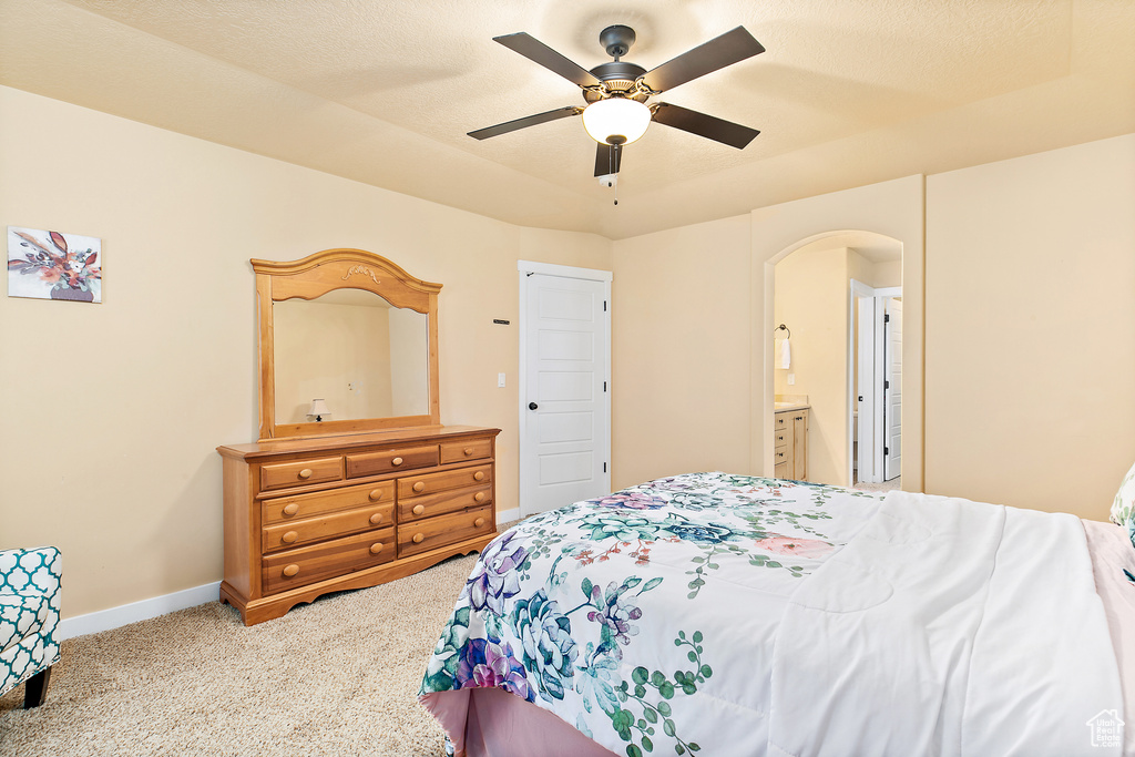 Carpeted bedroom featuring arched walkways, ceiling fan, ensuite bath, and baseboards