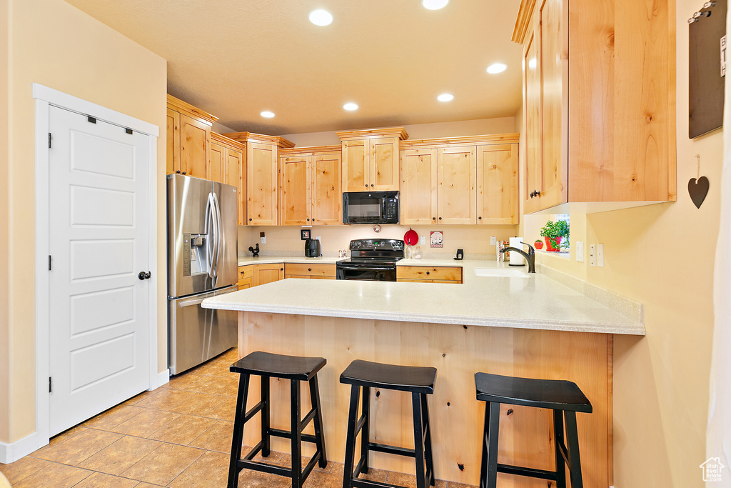 Kitchen featuring black appliances, light brown cabinets, light countertops, and a peninsula