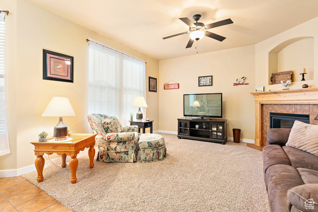 Carpeted living area with a tile fireplace, ceiling fan, and baseboards