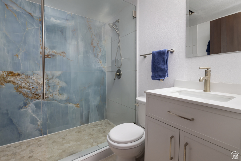 Bathroom with toilet, a marble finish shower, and vanity