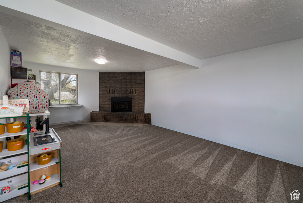 Recreation room featuring a textured ceiling, baseboards, carpet, and a fireplace