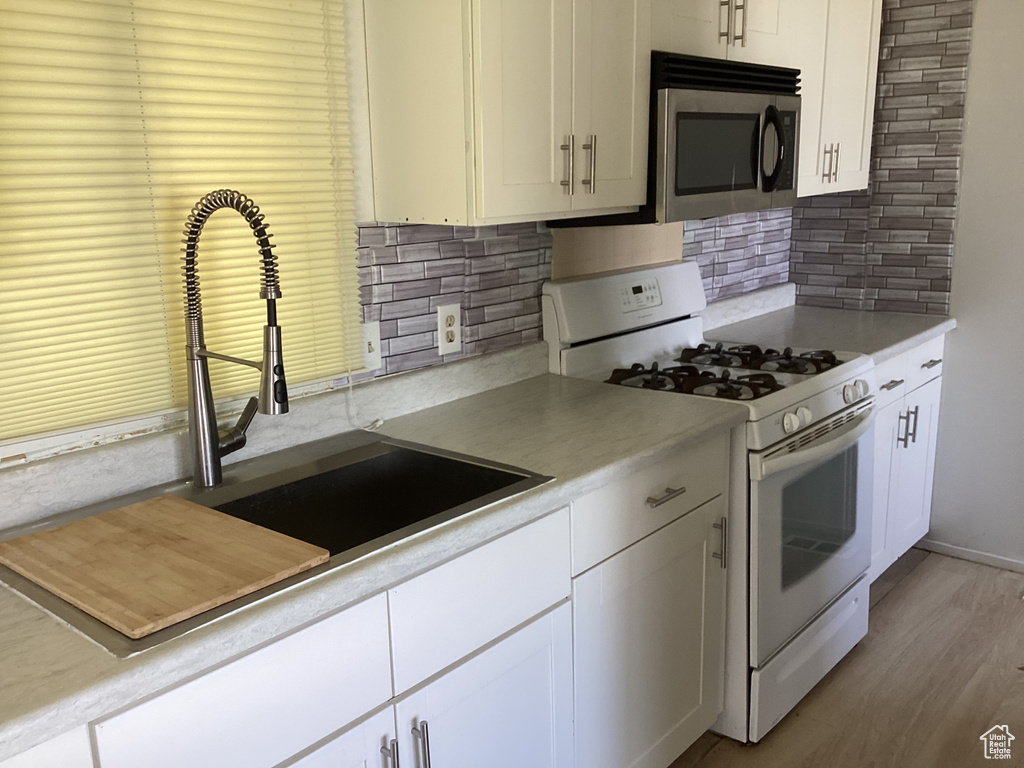 Kitchen featuring stainless steel microwave, white range with gas cooktop, a sink, and decorative backsplash