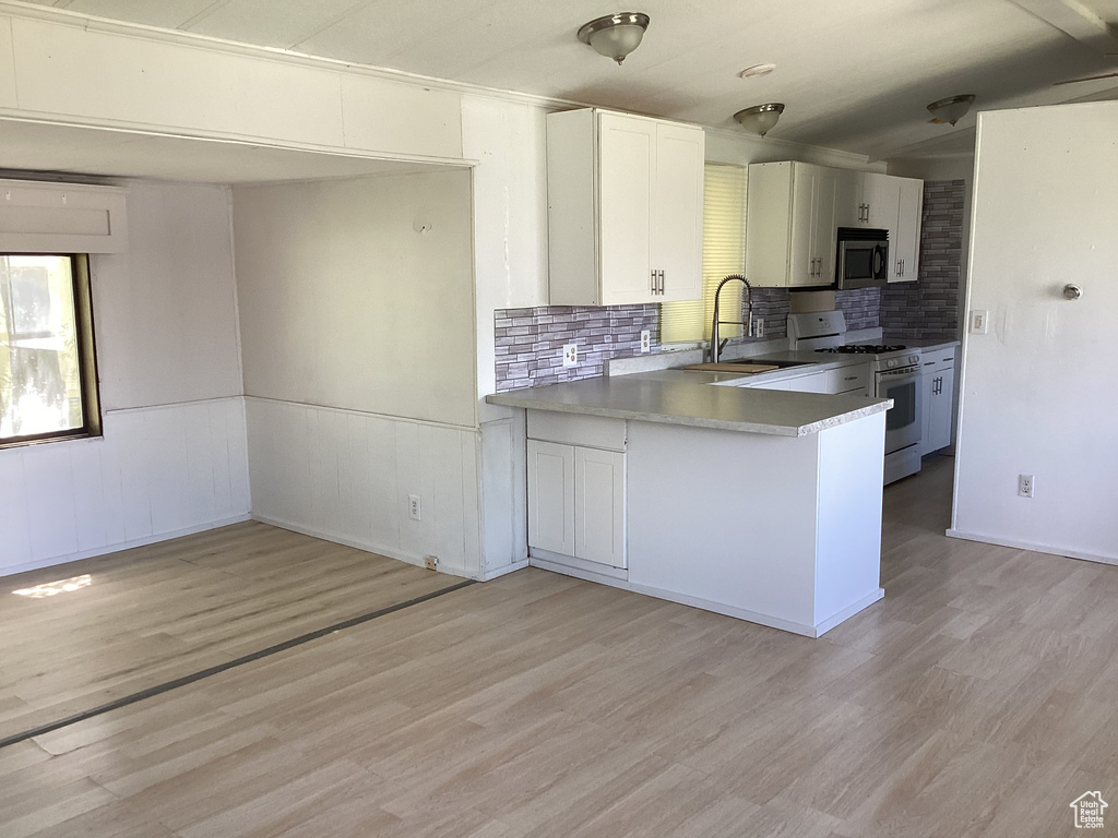 Kitchen with light wood-style flooring, decorative backsplash, stainless steel microwave, white range with gas cooktop, and a sink