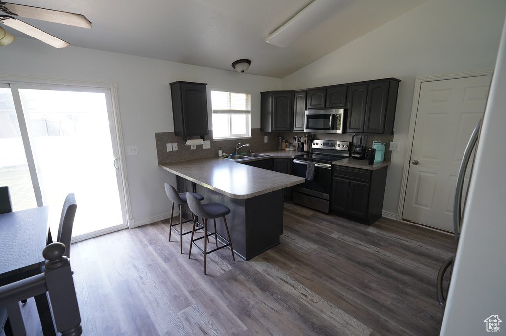 Kitchen with tasteful backsplash, a breakfast bar, a peninsula, appliances with stainless steel finishes, and lofted ceiling