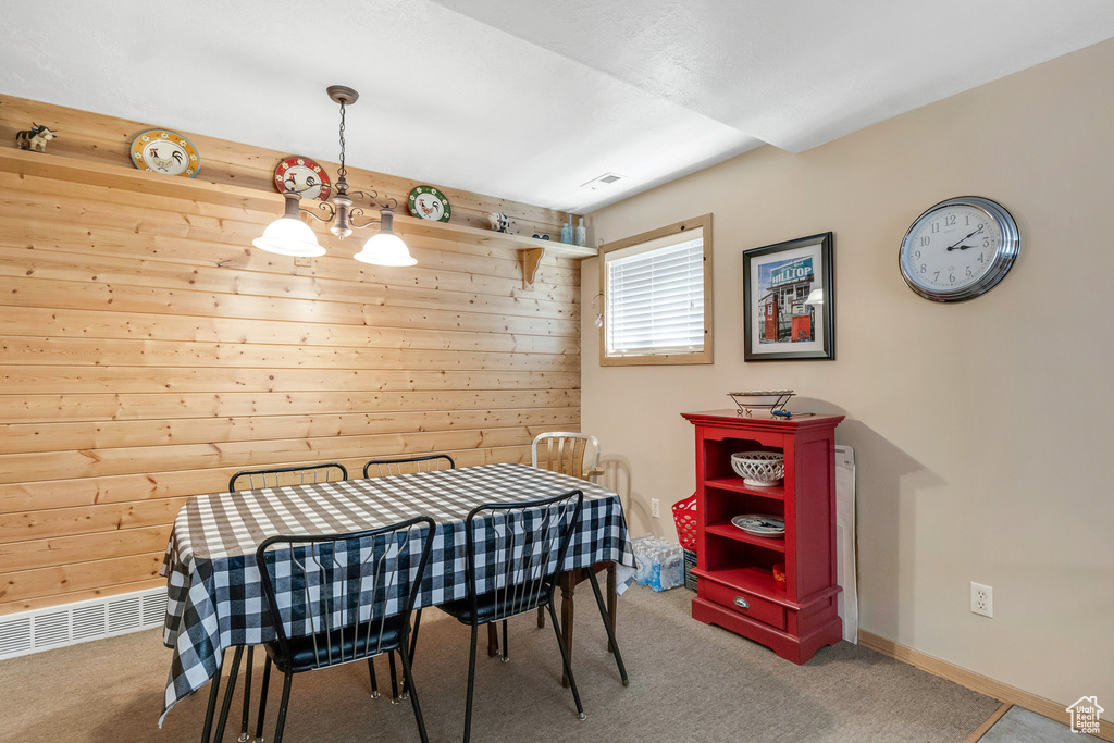 Dining room with wooden walls, carpet, visible vents, and a notable chandelier