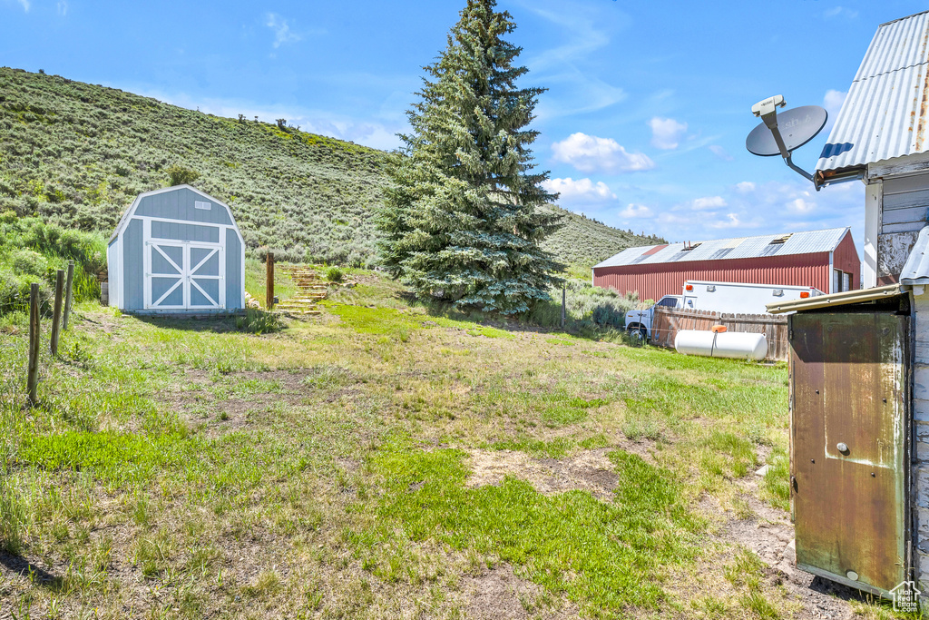 View of yard featuring an outdoor structure, a mountain view, a storage unit, and fence