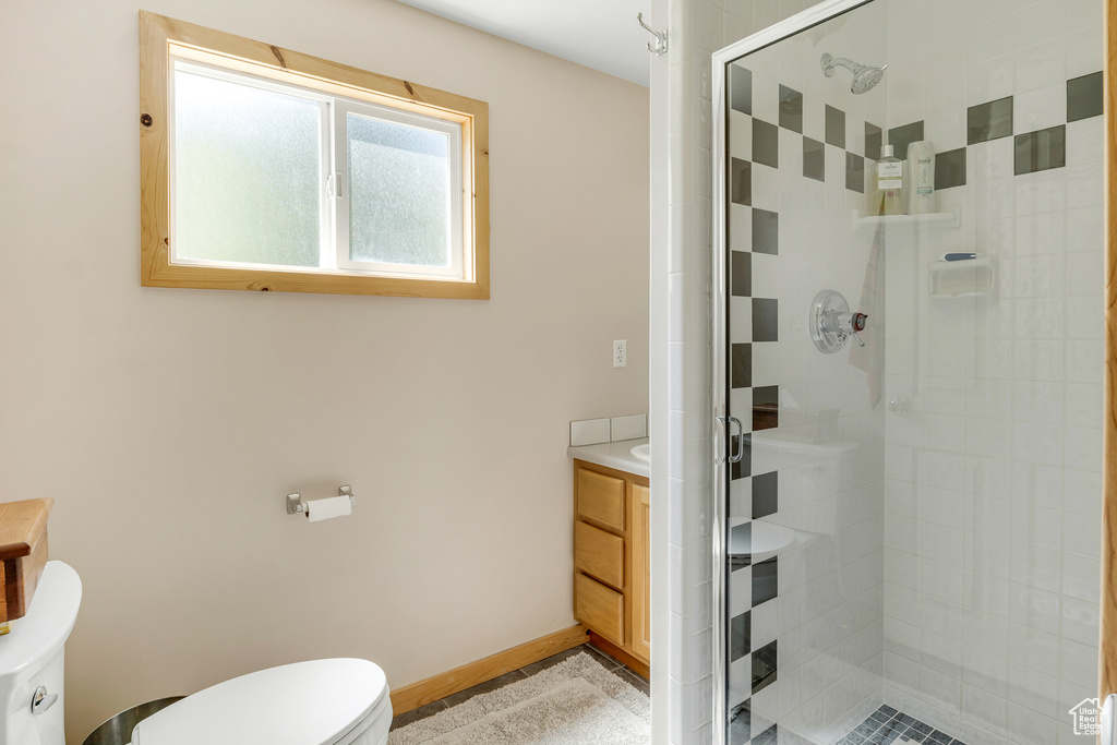 Full bath with toilet, a stall shower, vanity, and baseboards