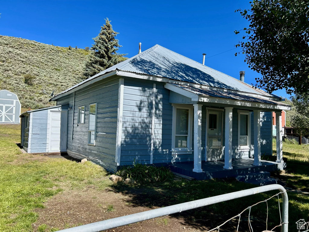 View of front facade with a porch, a front lawn, metal roof, an outbuilding, and a shed