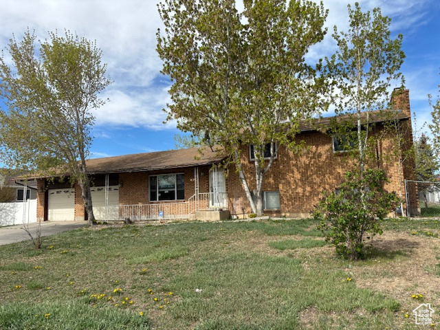 Split level home with a chimney, brick siding, a garage, driveway, and a front lawn