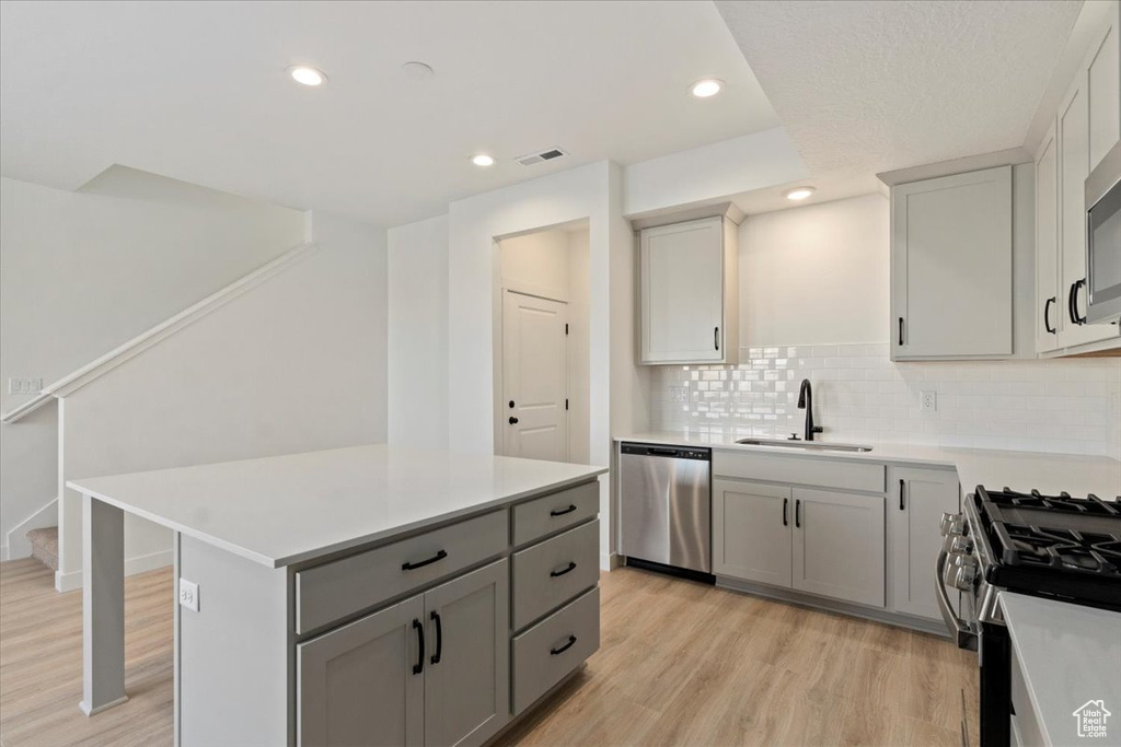 Kitchen with light wood-style flooring, a sink, gray cabinets, light countertops, and appliances with stainless steel finishes