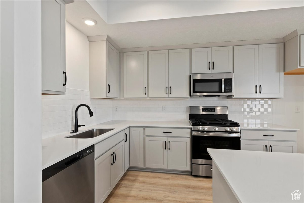 Kitchen featuring light countertops, decorative backsplash, stainless steel appliances, and a sink