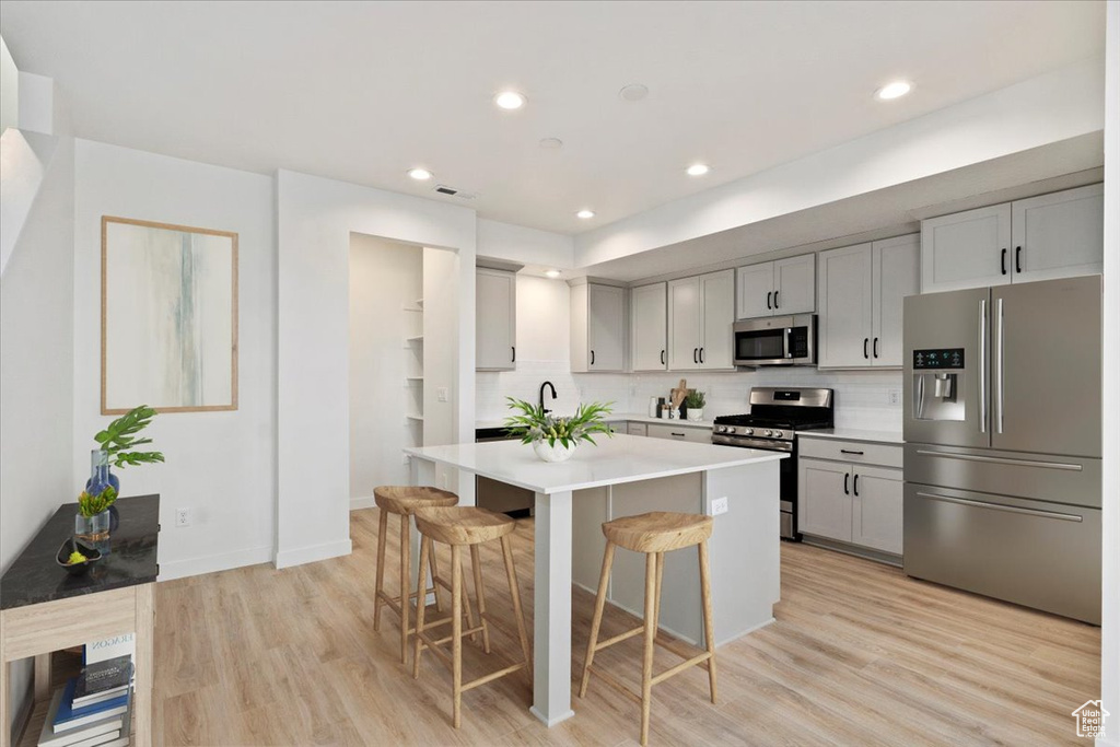 Kitchen with light wood finished floors, stainless steel appliances, a center island, a kitchen bar, and light countertops
