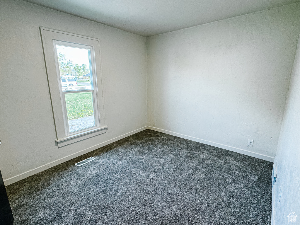 Empty room featuring dark colored carpet, visible vents, and baseboards