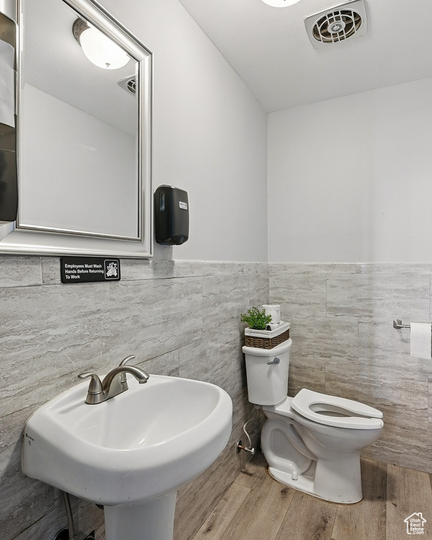 Bathroom featuring a sink, toilet, tile walls, visible vents, and wood finished floors