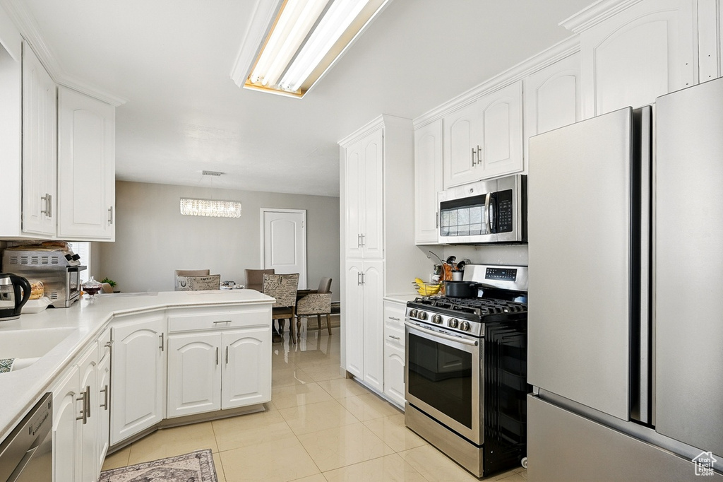 Kitchen with stainless steel appliances, light countertops, light tile patterned floors, a peninsula, and white cabinetry