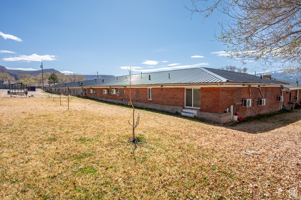 View of side of property featuring brick siding, a yard, metal roof, and a mountain view