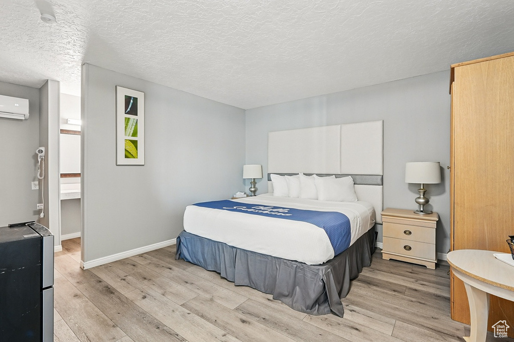 Bedroom featuring baseboards, light wood finished floors, a textured ceiling, and a wall mounted AC