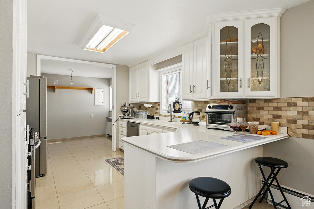 Kitchen with white cabinets, backsplash, a sink, a peninsula, and a breakfast bar area