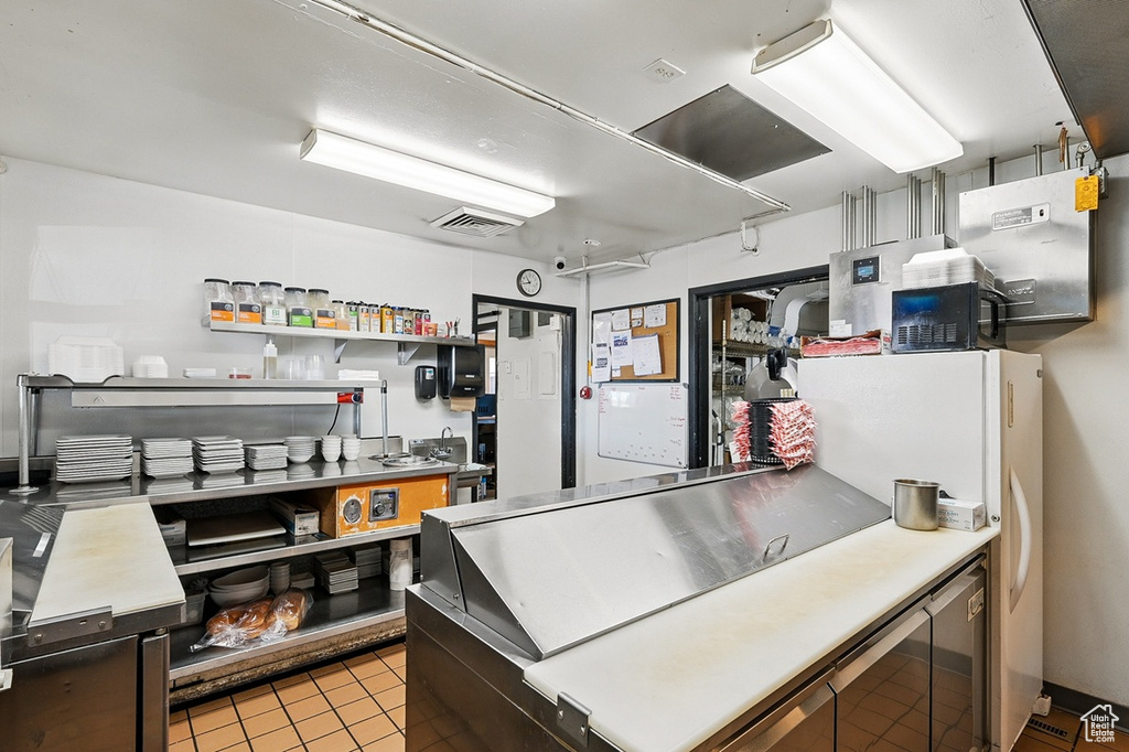 Kitchen featuring black microwave, freestanding refrigerator, visible vents, and light tile patterned floors