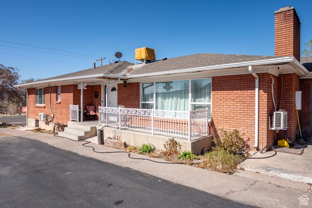 Ranch-style home featuring a chimney, a shingled roof, covered porch, brick siding, and ac unit