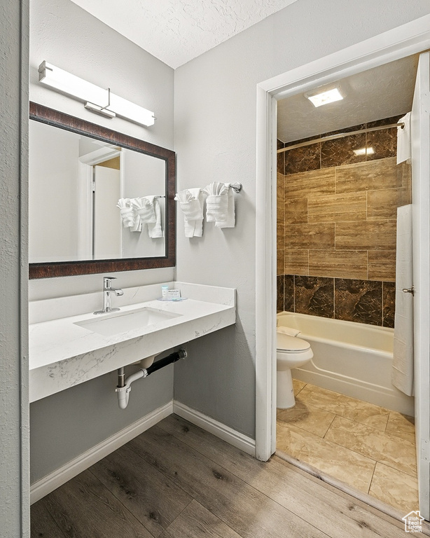 Full bath with wood finished floors, shower / bathtub combination, toilet, a sink, and a textured ceiling