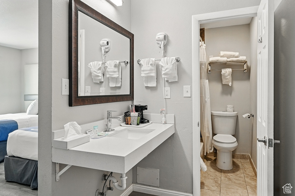 Bathroom with curtained shower, toilet, a sink, baseboards, and ensuite bathroom