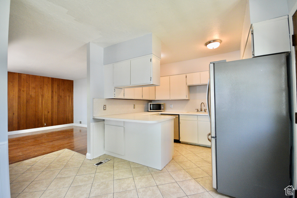 Kitchen with appliances with stainless steel finishes, light countertops, a sink, white cabinetry, and a peninsula