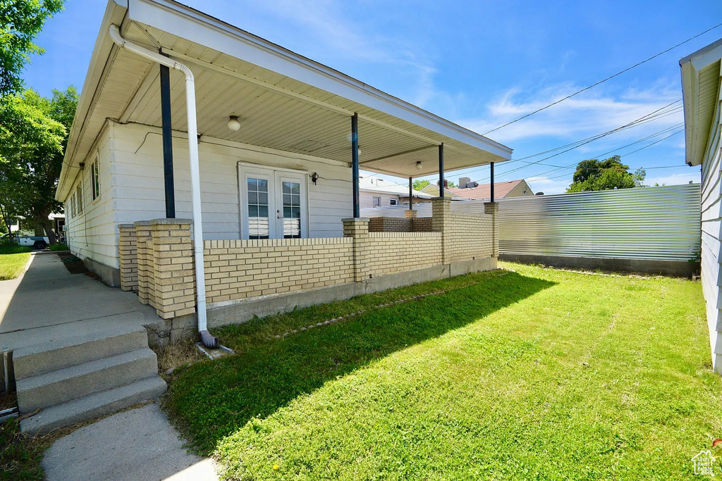 View of side of property with a porch, a lawn, fence, and brick siding