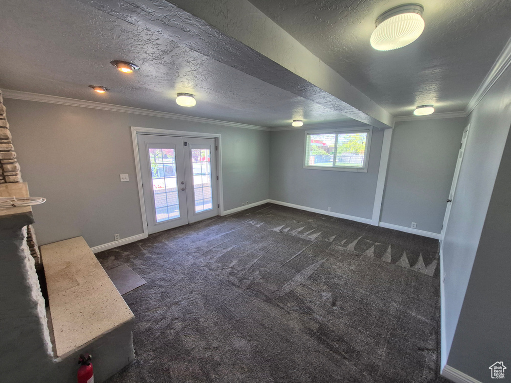 Below grade area featuring dark carpet, a textured ceiling, crown molding, baseboards, and french doors