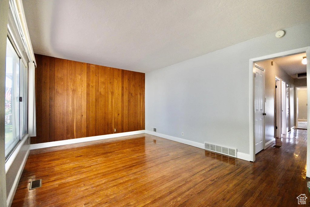 Empty room featuring baseboards, visible vents, wood finished floors, and wood walls