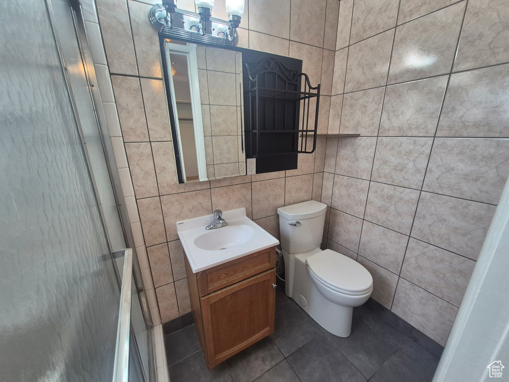 Full bathroom with tile patterned floors, tile walls, an enclosed shower, toilet, and vanity