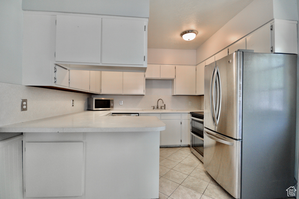 Kitchen featuring light tile patterned floors, appliances with stainless steel finishes, light countertops, a sink, and a peninsula
