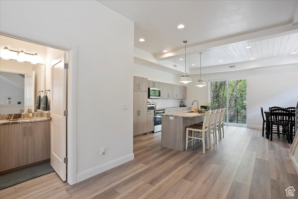 Kitchen with light wood-style flooring, a sink, appliances with stainless steel finishes, a breakfast bar, and modern cabinets