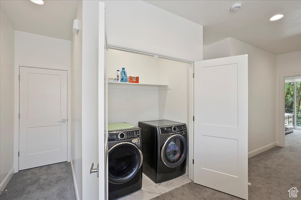 Clothes washing area with light colored carpet, washing machine and clothes dryer, laundry area, and baseboards