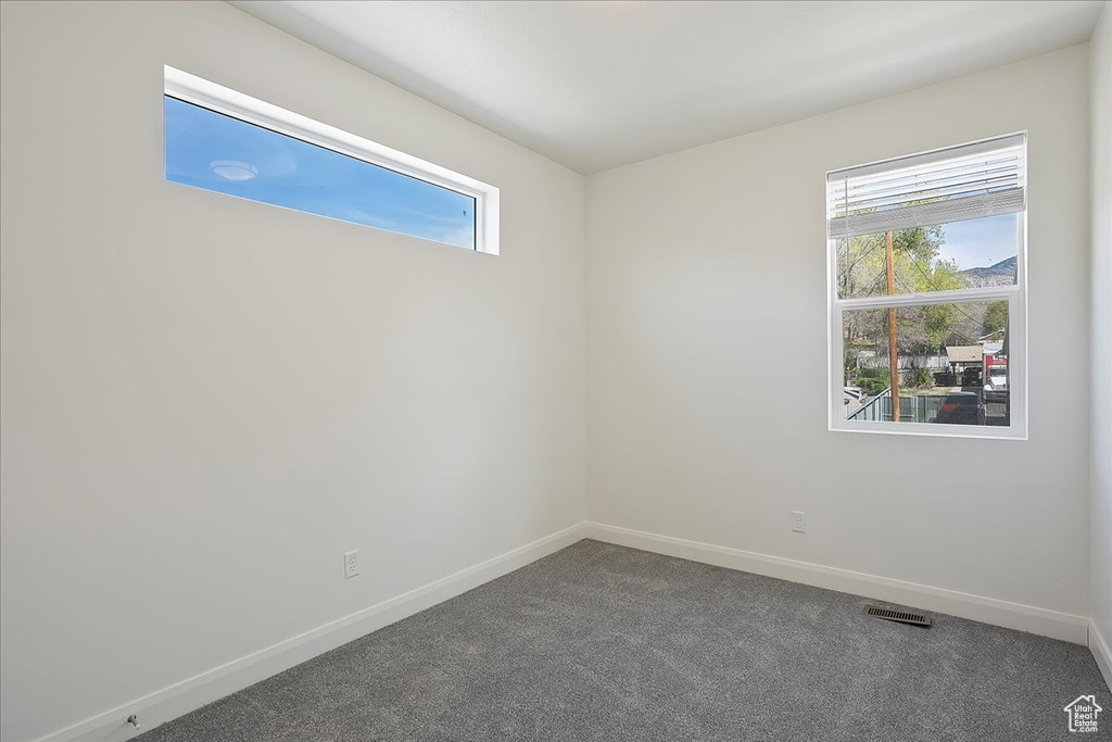 Unfurnished room featuring visible vents, baseboards, dark colored carpet, and a healthy amount of sunlight