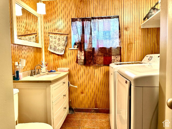 Laundry area featuring separate washer and dryer, a sink, wood walls, and laundry area
